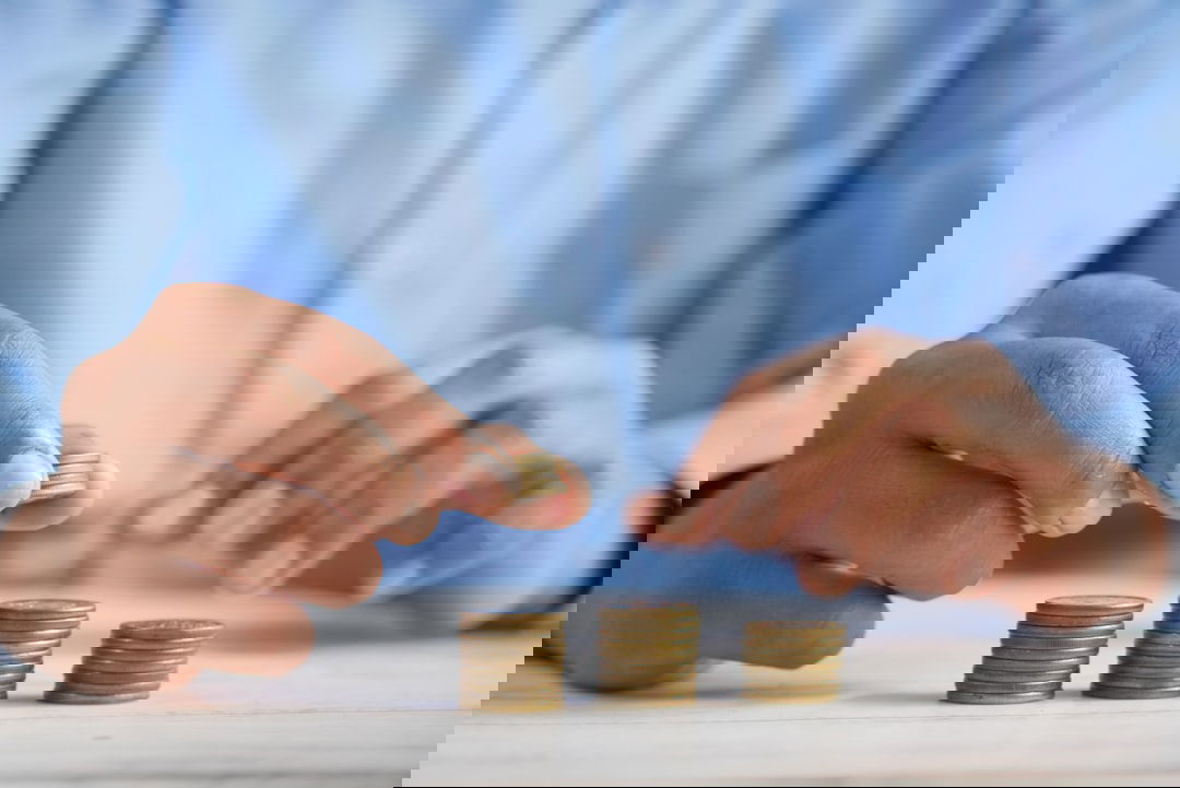 Eine Person stapelt Münzen als Symbol zum Sparen